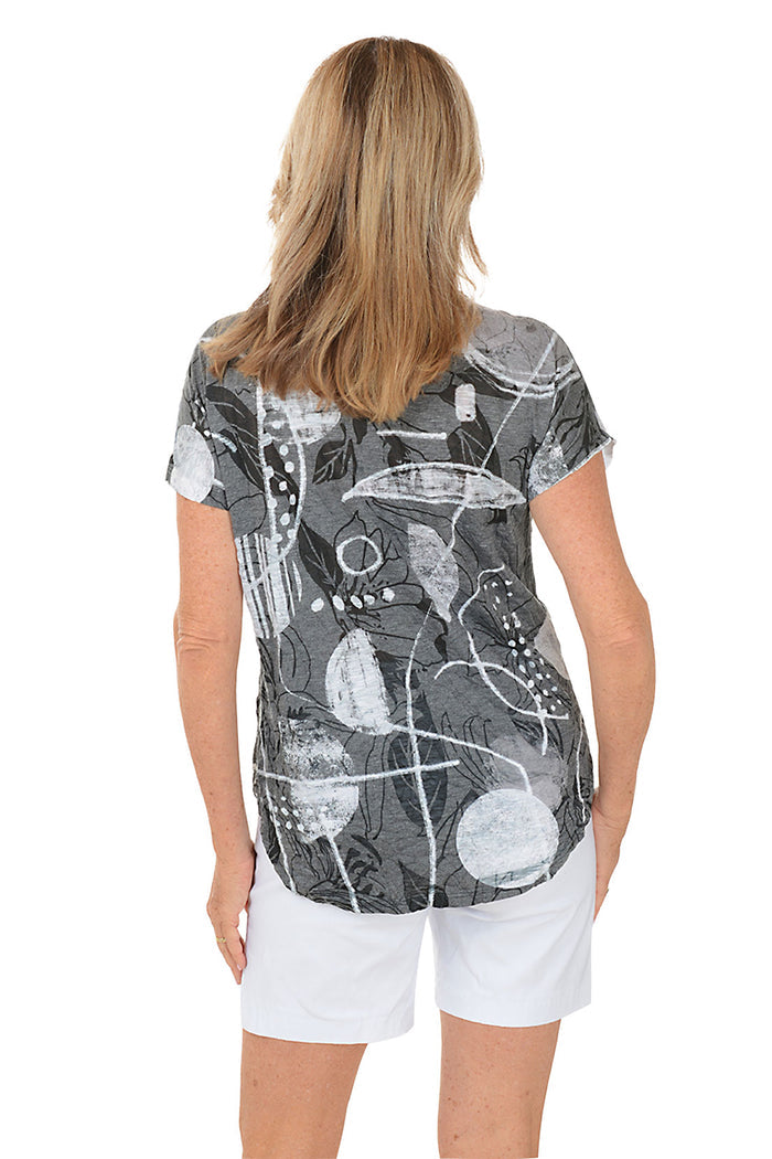 A woman wearing a black and white short sleeve top with an abstract print. Back shot.