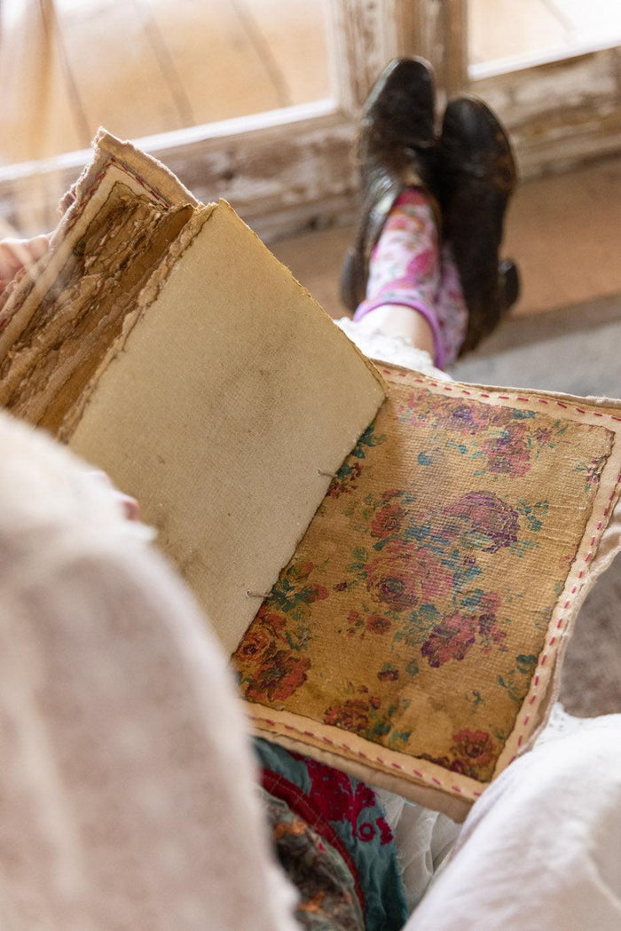 Woman in Magnolia Pearl artisan clothing and floral socks reading vintage floral book indoors