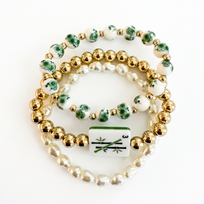 Set of three beaded bracelets with gold, green, and white beads on a white background