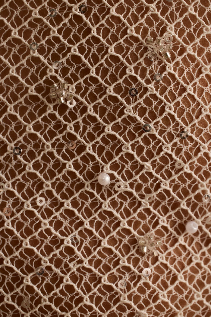 Close-up of ivory open-weave mesh scattered with pearls and sequins on skin.
