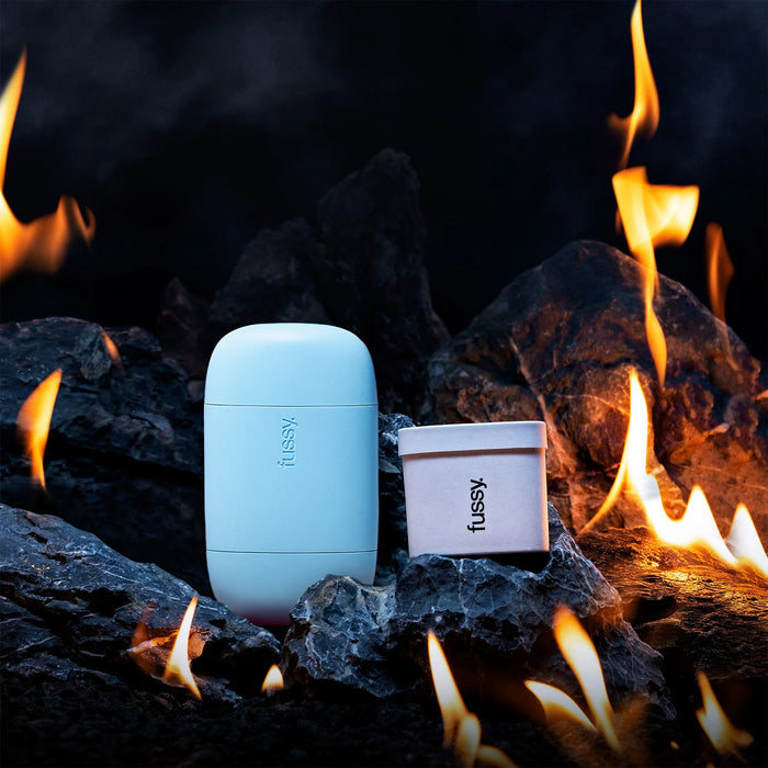 Fussy's natural, refillable deodorant starter pack with Blue case, set against a backdrop of flaming coals.