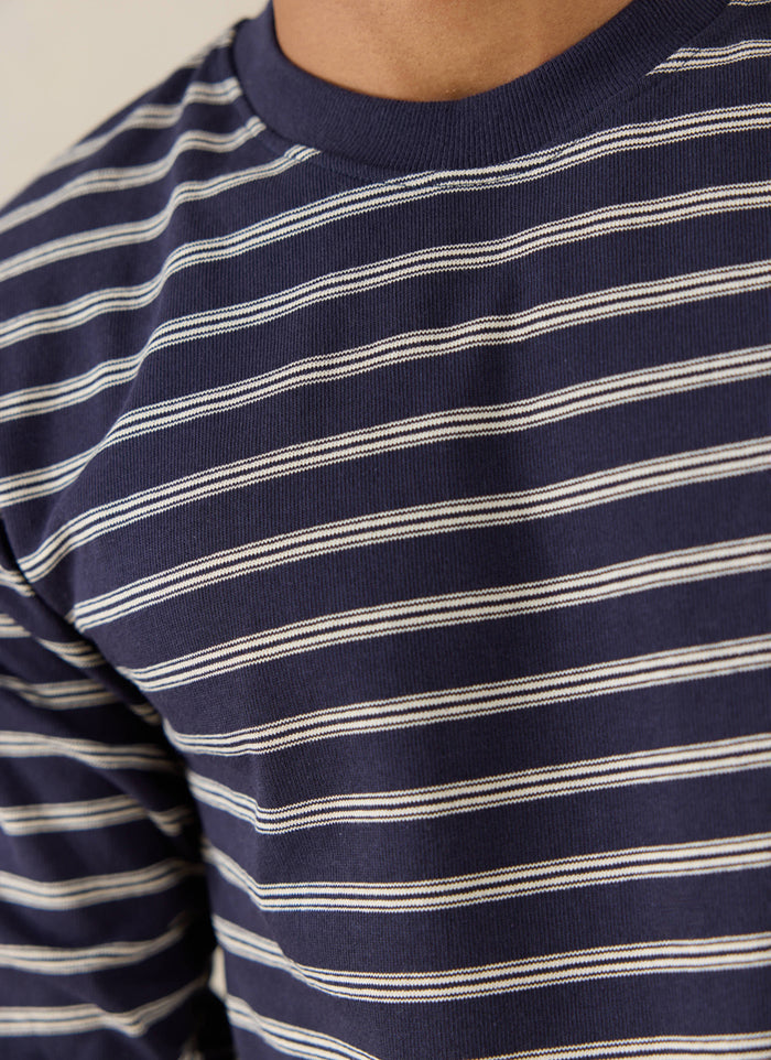 Close-up of a model wearing the navy stripe Percival Arlo long sleeve Breton T-shirt, showing the crew neck and pattern.