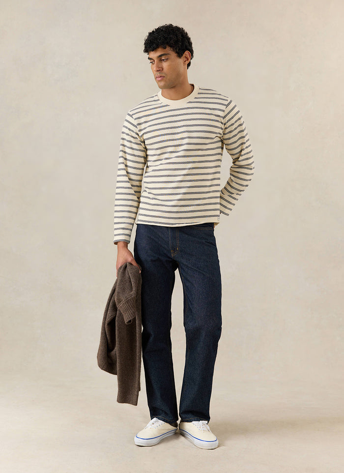 A model wears the white stripe Arlo Breton long sleeve T-shirt from Percival, styled with dark jeans in a studio setting.