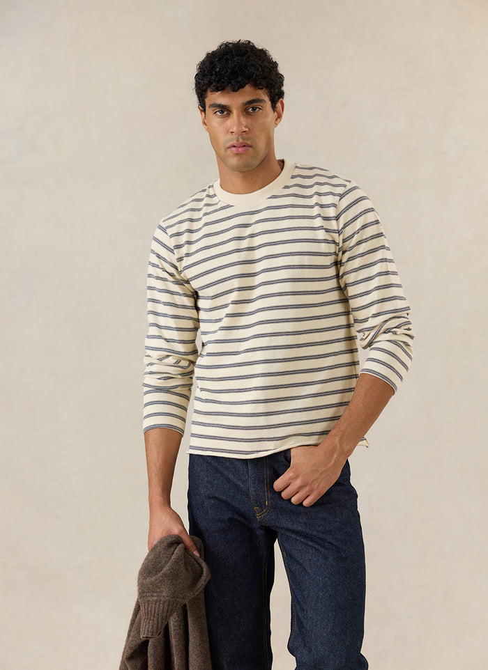 A model wears the Percival Arlo white stripe long sleeve Breton T-shirt with blue jeans in a studio.