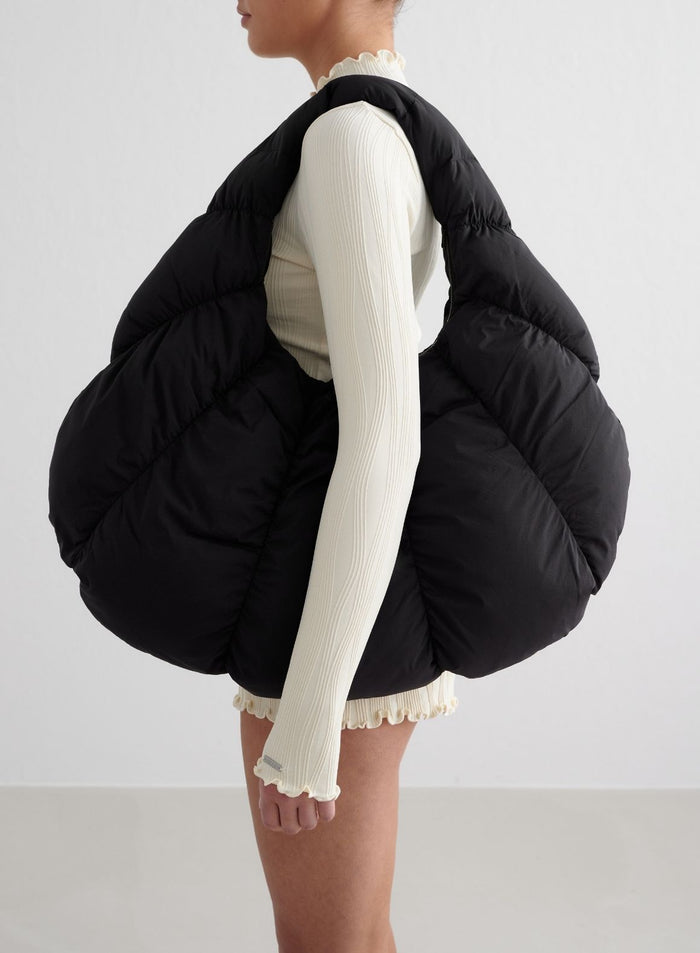 Oversized black puffy Croissant Bag from aim'n with a quilted nylon texture, worn over the shoulder.