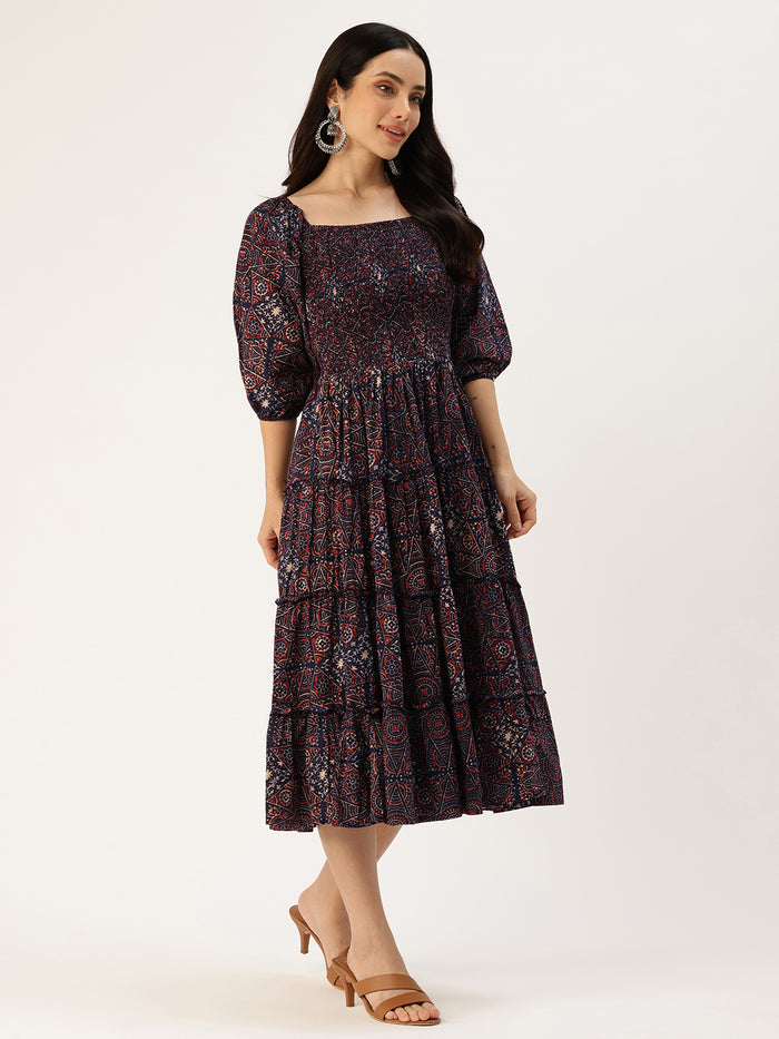 Woman in a dark floral dress standing on a stone path with pink flowers and a building in the background, Blue Floral Printed Cuffed Sleeves Dress, midi dress, dress, women’s western wear, party wear dress, casual wear dress