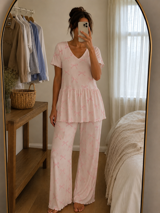 Woman wearing a blush pink ribbon print ribbed knitted cotton peplum night suit with V-neck top and matching straight-fit lounge pants by Irah Vastra.
