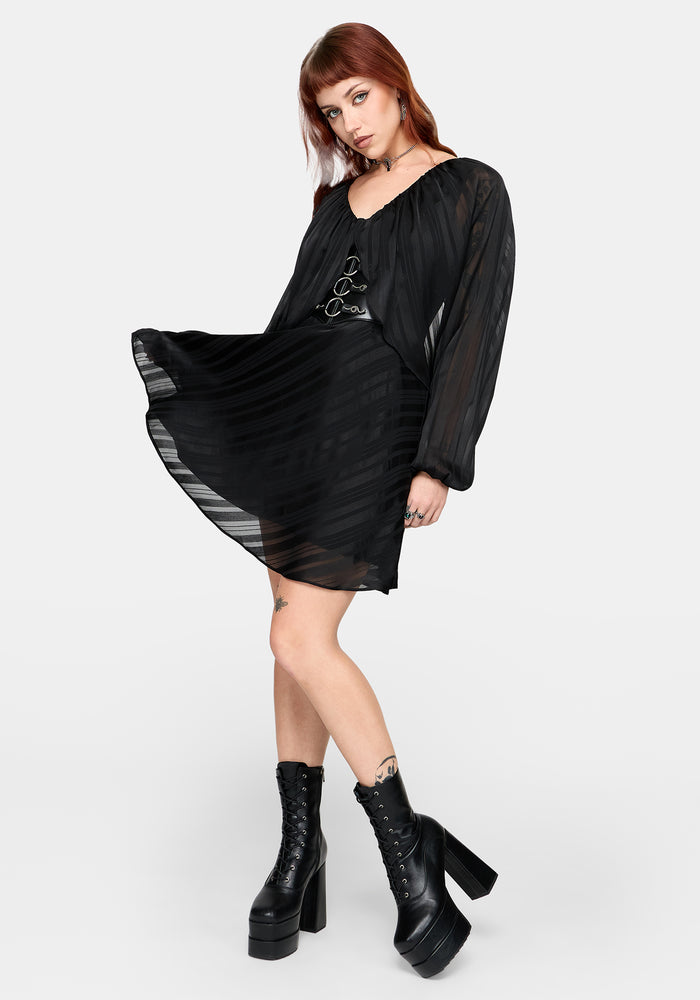 Woman wearing a black dress with long sleeves and platform boots on a white background