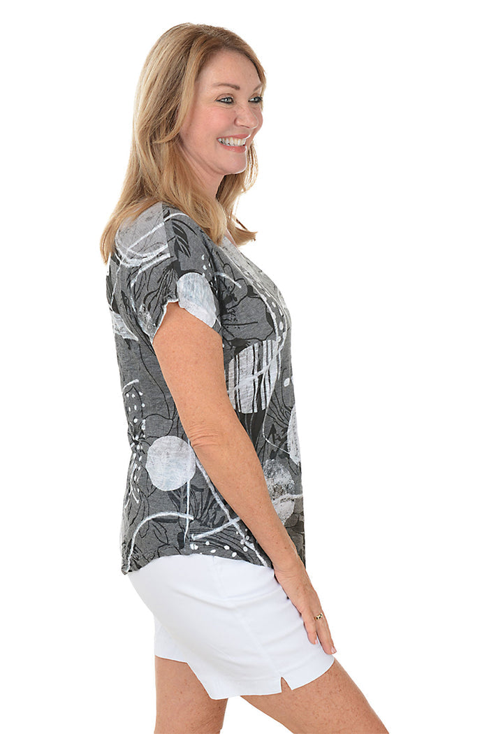 A woman wearing a black and white short sleeve top with an abstract print. Side shot.