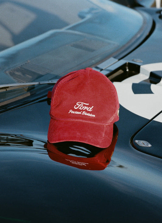 Red corduroy Ford x Percival trucker cap with white embroidery, resting on a black car bonnet.