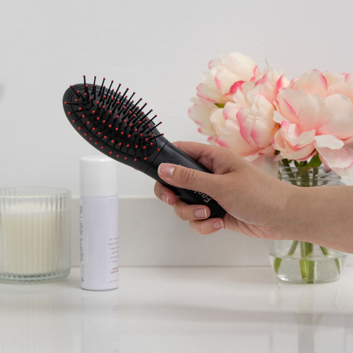 Zadro MB05 705004419734 environment photo hand holding brush, detangling hair brush with feelz good massager in front of a real life setting