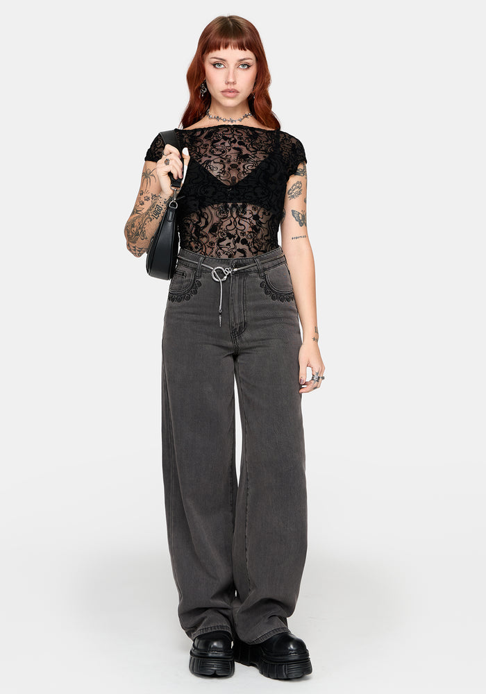 Woman wearing a black lace top and gray straight leg jeans on a white background