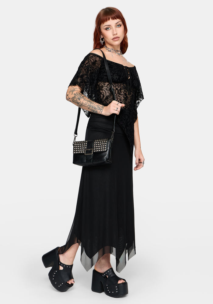 Woman wearing a black lace top and skirt with studded shoes and studded handbag on a white background