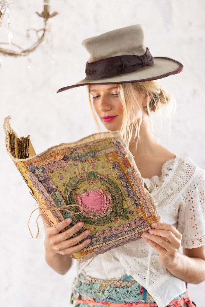 Woman in Magnolia Pearl artisan hat and lace blouse reading a whimsical, vintage-style fabric book
