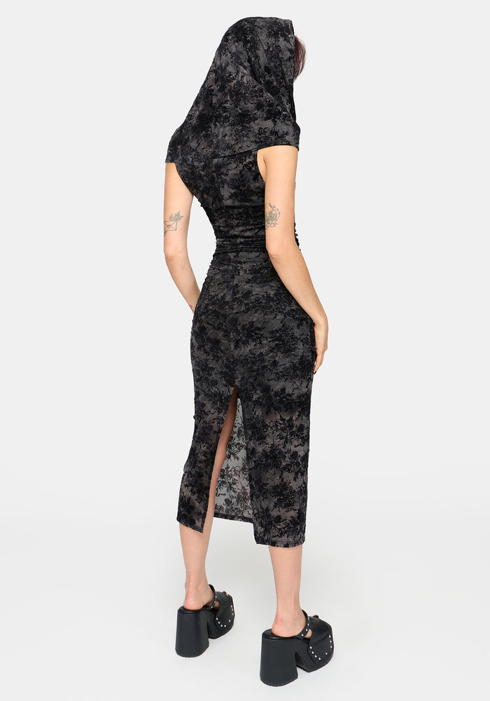 A woman shown from the back wearing a short-sleeve black and gray floral-patterned midi dress with a high slit and a matching head covering, paired with black platform sandals, against a light gray studio background.