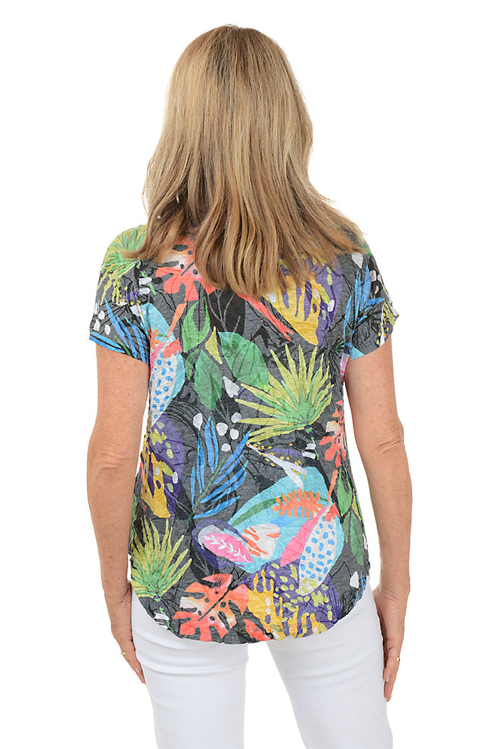 A woman wearing a multi colored tropical print short sleeve top. Back shot.