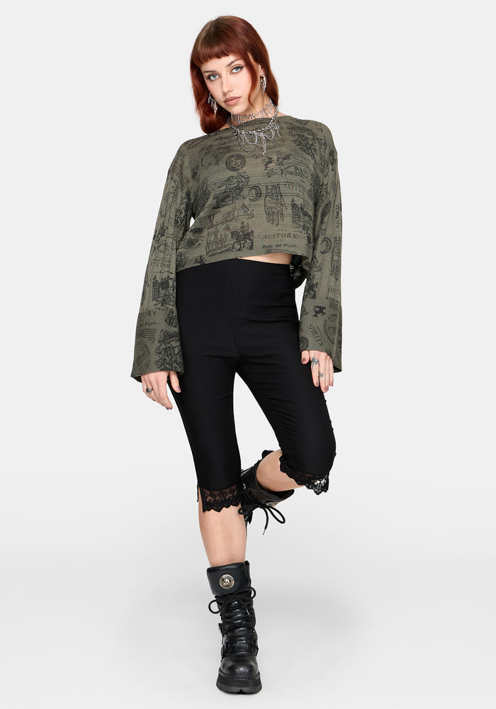 Woman wearing a patterned green jumper and black pants against a plain background