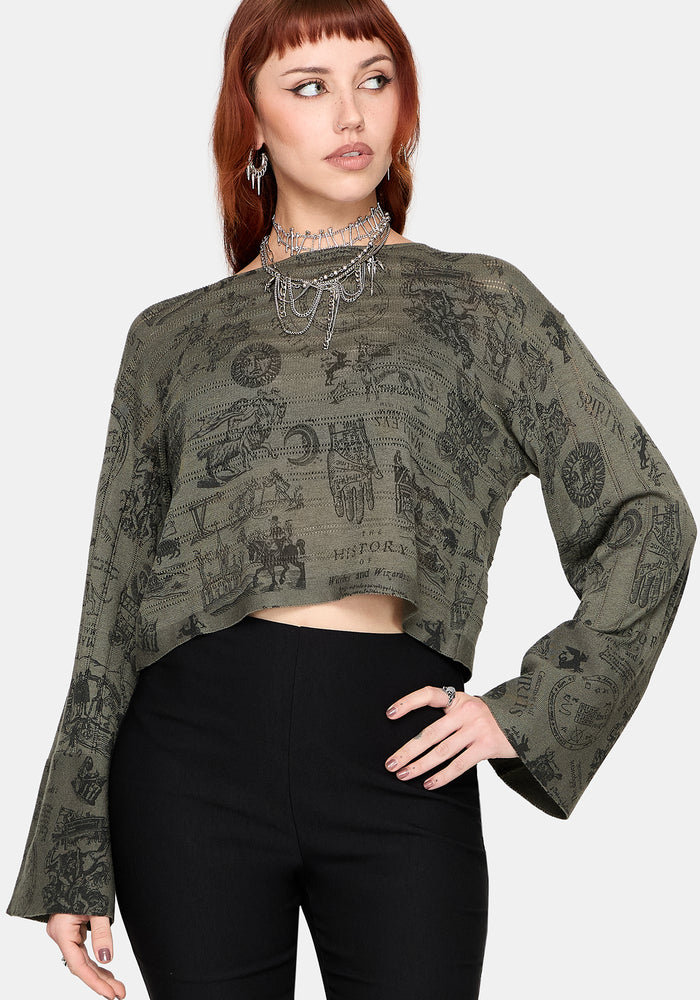 Woman wearing a patterned green jumper and black pants against a plain background