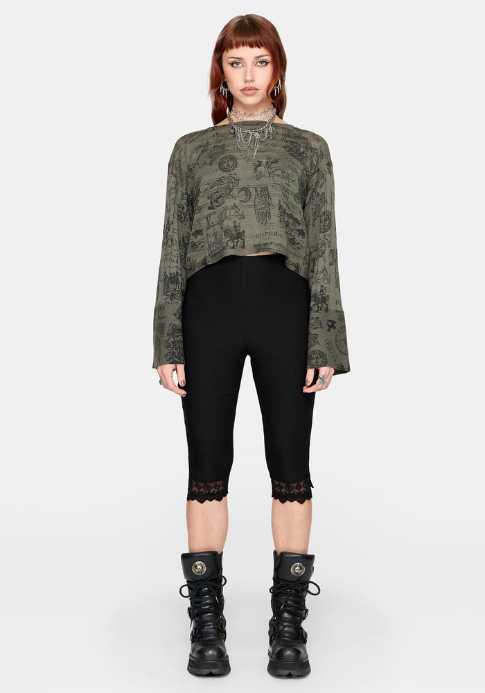 Woman wearing a patterned green jumper and black capri leggings against a plain background