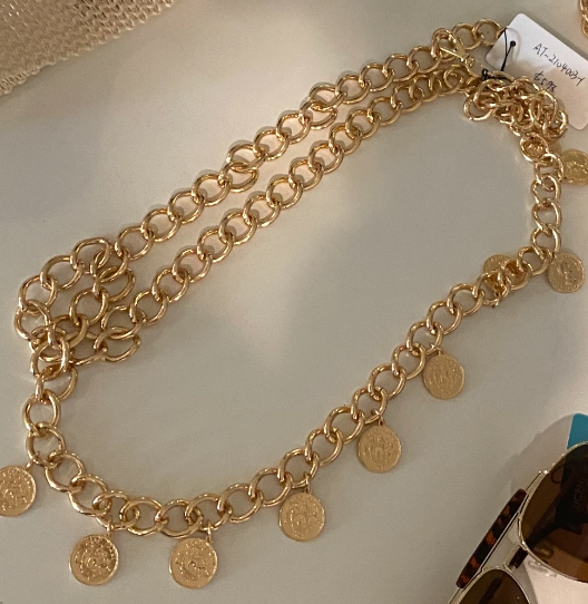 Gold layered curb chain belt with hanging coin pendants laid flat on cream surface.
