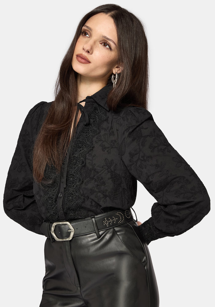 Woman wearing a black long sleeve lace detail blouse with a plain background