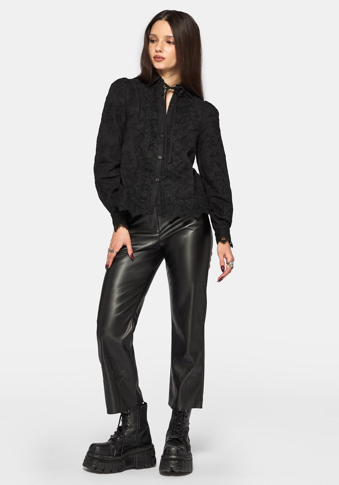 Woman wearing a black long sleeve lace detail blouse with black leather pants on a plain background