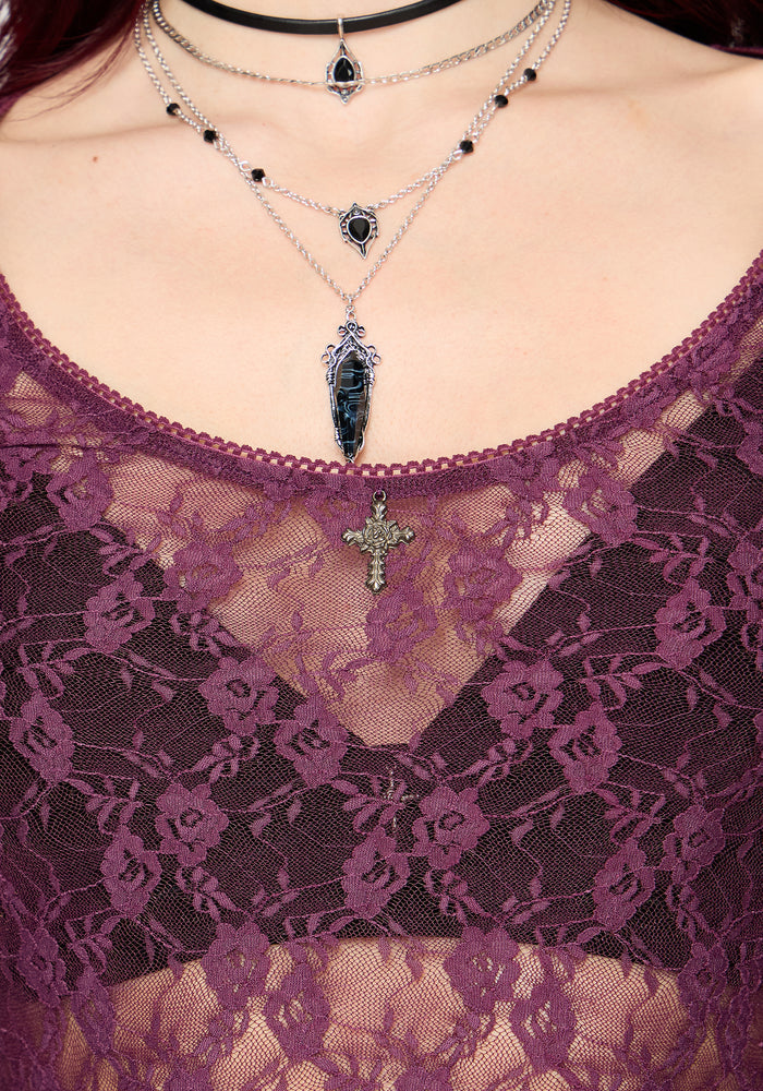 Close-up of a person wearing layered necklaces with a purple lace top.