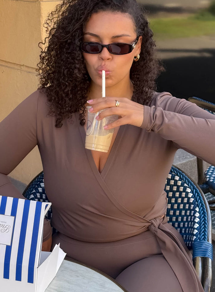 Macchiato aim'n Shape Seamless Wrap Long Sleeve top with a wrap-around tie worn at an outdoor cafe.