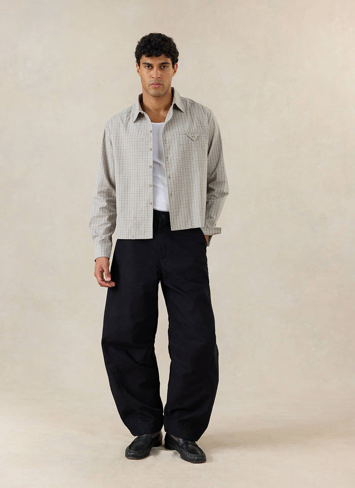 A model wears the black Percival Milo Relaxed Barrel Leg Trousers, styled with a checkered shirt and white tank top.
