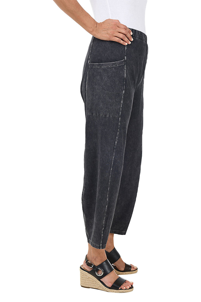 A side shot of a model wearing a black mineral wash pull-on ankle pants with an elasticized waistband, dual side pockets, and tapered leg design.