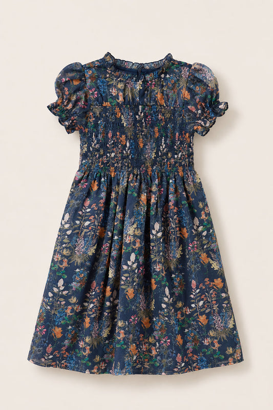 The Ivy City Co Mini Leonora Dress in Midnight Autumn Bouquet is a short-sleeved, knee-length dress featuring a navy background with a colorful floral print, smocked bodice, puff sleeves, ruffled collar, and gathered skirt. It is shown laid flat on a light background.