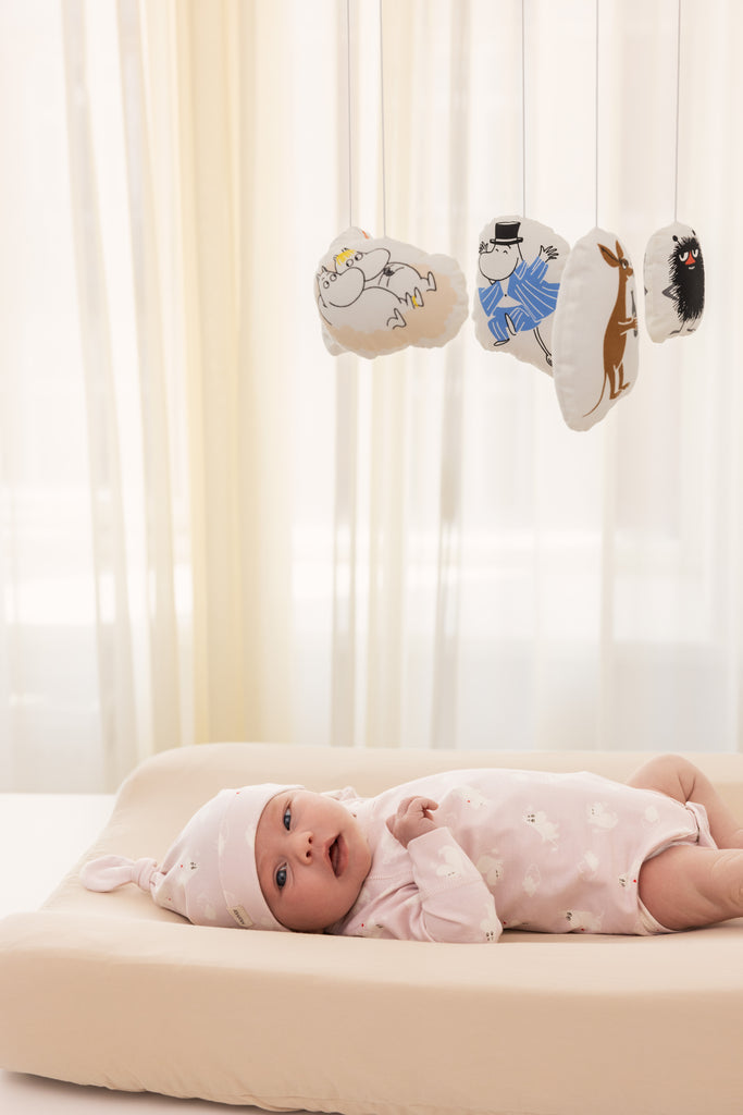 Babymobil med Moomin-figurer ophængt i stof, set over babys seng.