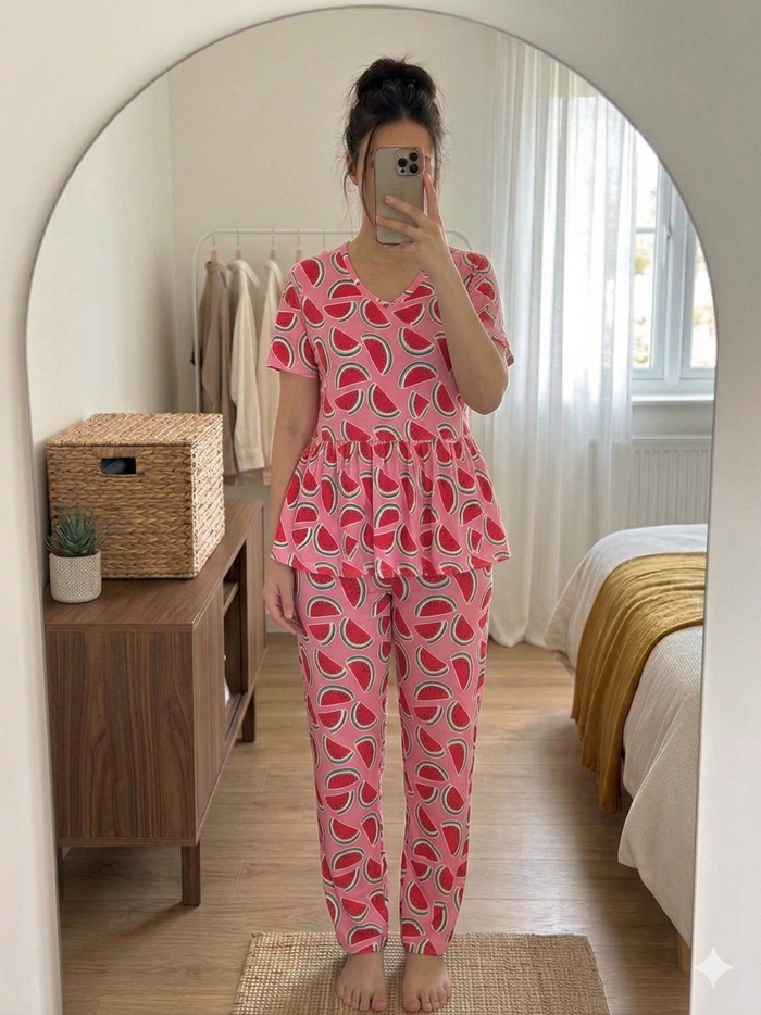 Woman wearing pink watermelon print peplum night suit set with short sleeves and full-length pants, taking a mirror selfie in a cozy bedroom.