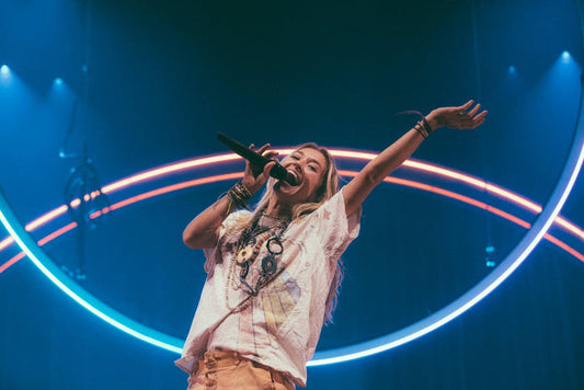 Woman performing on stage with microphone, wearing artisan boho t-shirt and layered necklaces