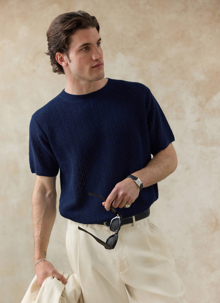 The navy Percival Siena Knitted T Shirt, featuring a textured open-work cotton knit, worn by a model with cream trousers.