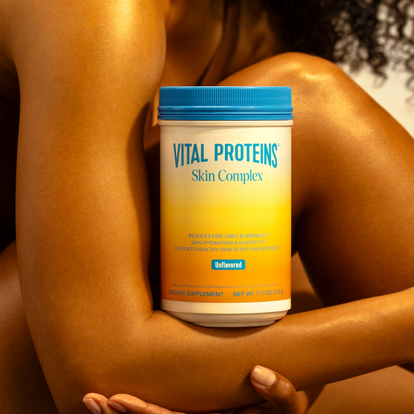 Container of Skin Complex - Unflavored | Vital Proteins dietary supplement held between the arms of a person with smooth skin, highlighting skincare and wellness benefits.