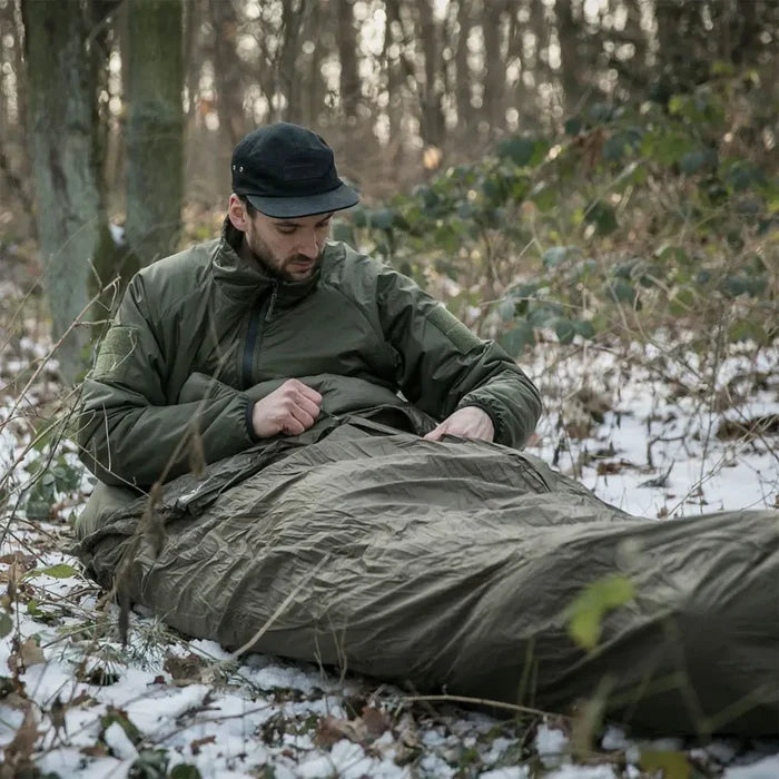 Lifestyle shot of a man using a Snugpak bivi bag in olive colour with his sleeping bag outdoors in winter