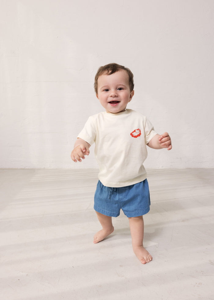 Baby wearing a white T-shirt with Mumin print and denim shorts.