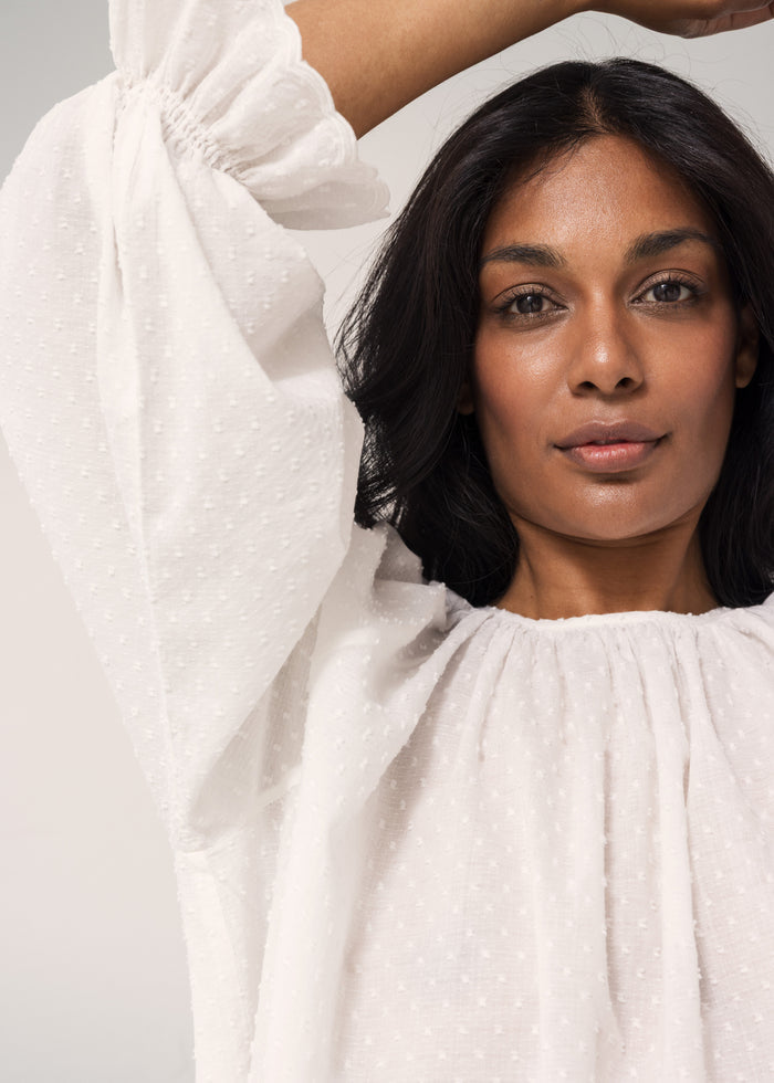 White blouse with round neck and creased detail, as well as puff sleeves with soft ruffles.