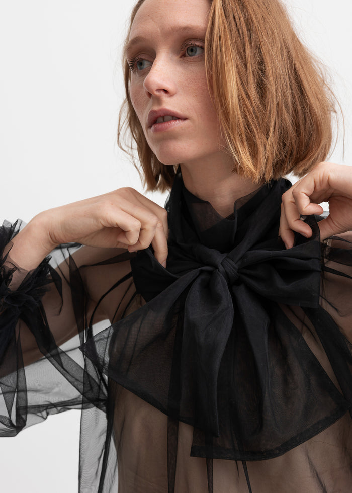 Woman wearing black transparent tulle blouse with large bow