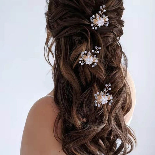 A woman with long, wavy brown hair styled half-up is adorned with three elegant pearl and crystal floral hairpins, on a plain light background.