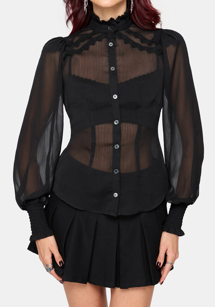 A model wearing a black sheer long-sleeve blouse with lace trim and a black pleated mini skirt, shown against a light gray studio background.
