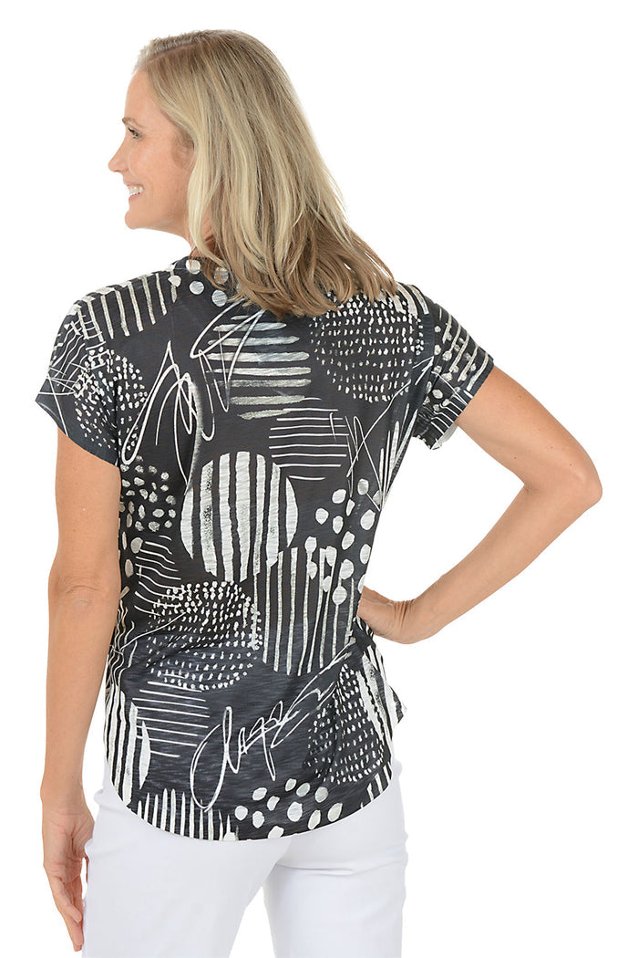 A woman wearing a black and white short sleeve v-neck shirt with an abstract design. Back shot.